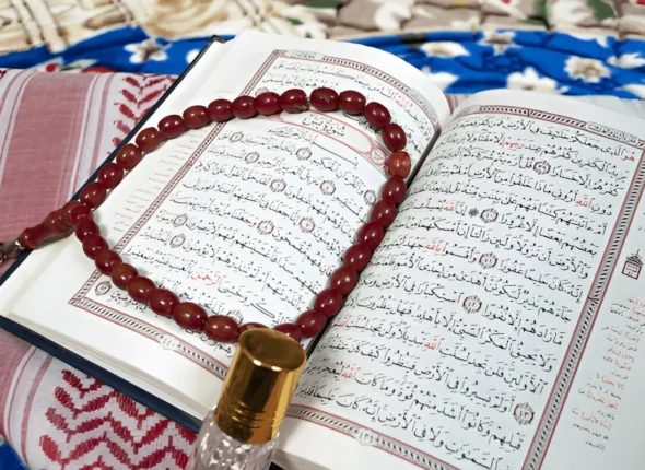Holy Quran with Tajweed, a rosary, and a bottle of perfume on a table.
